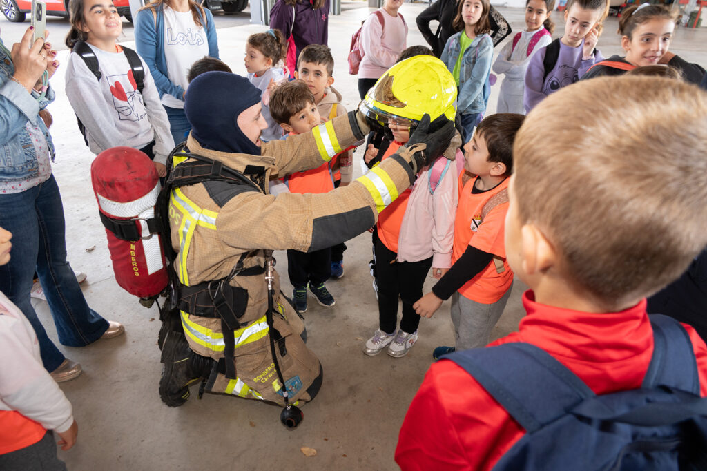 Un bombero coloca un casco a un niño, acompañados de otros niños y niñas